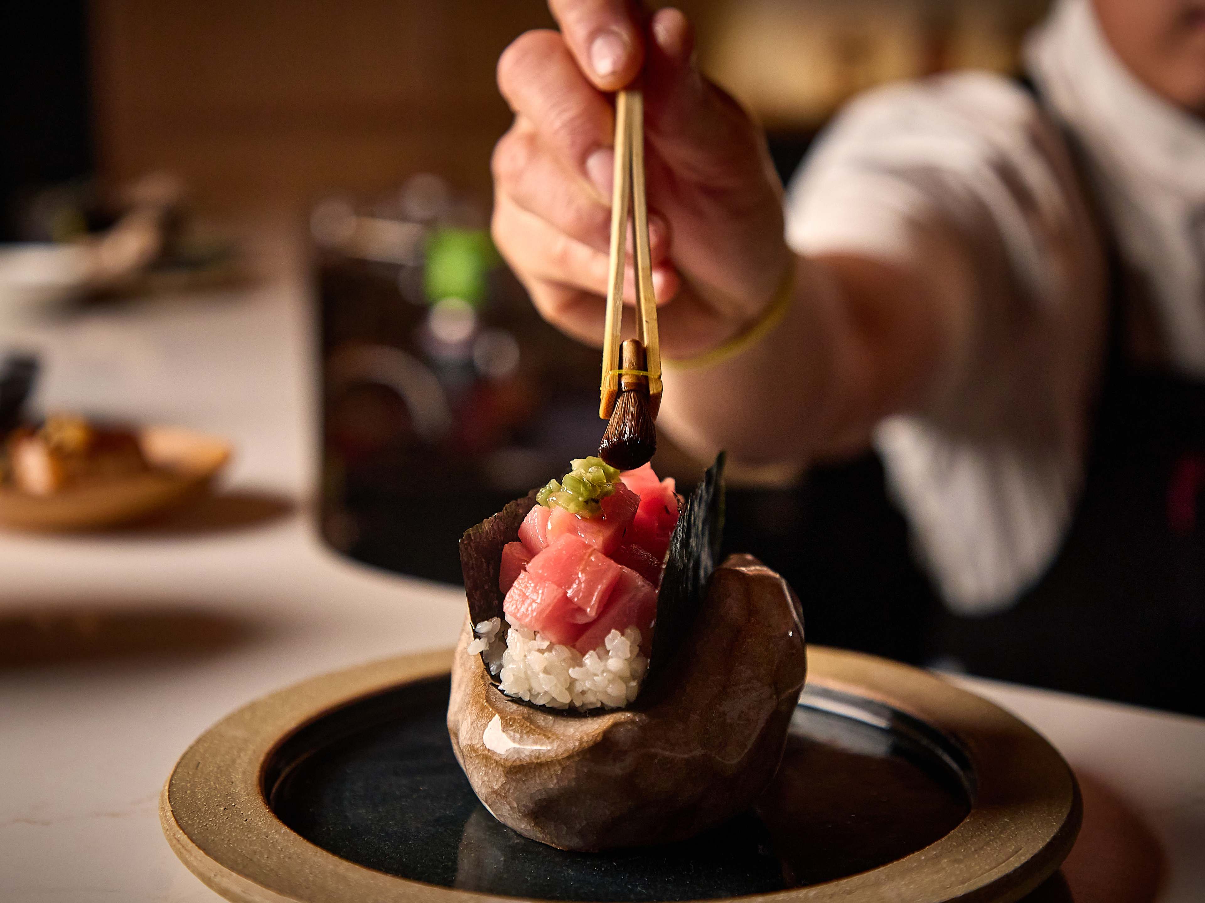 A hand using chopsticks to garnish a tuna handroll.